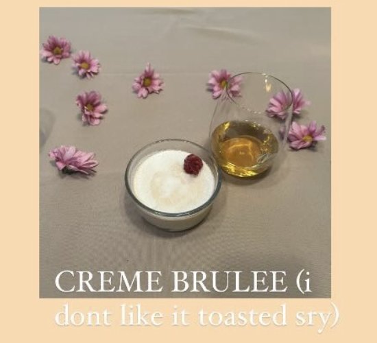 A crème brûlée with a raspberry on top, served with a glass of dessert wine.