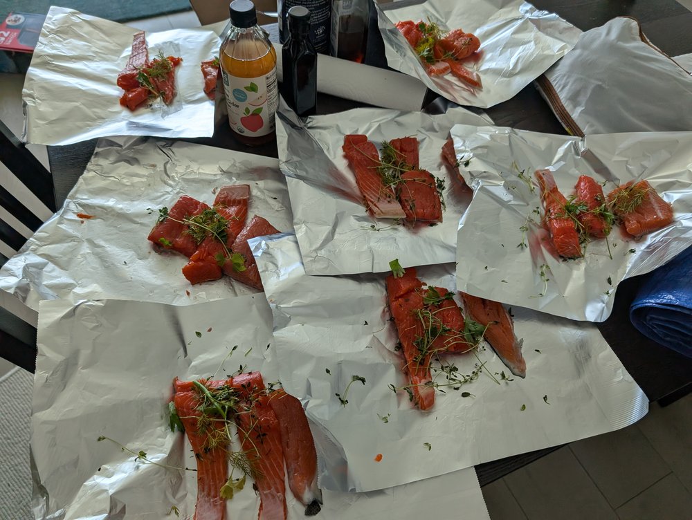 Raw salmon portions topped with herbs, laid out on individual foil sheets ready to cook.