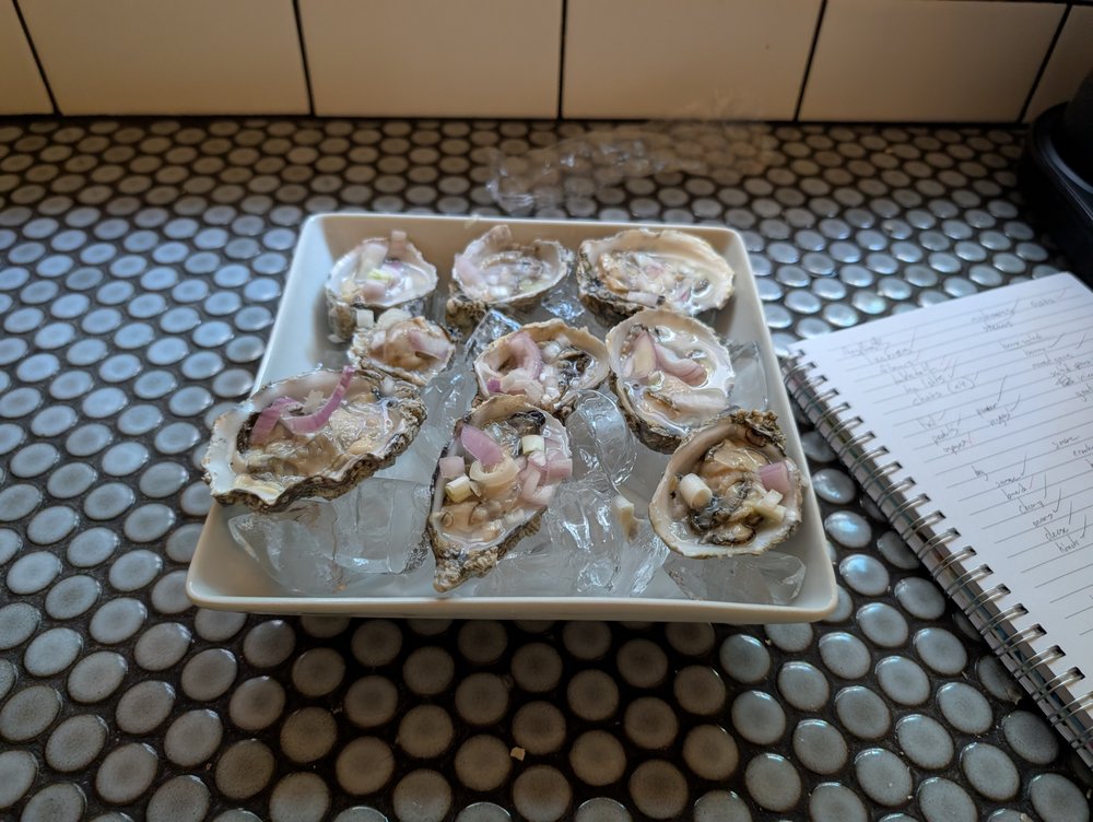 Seven oysters plated on ice next to a spiral notebook of tasting notes.