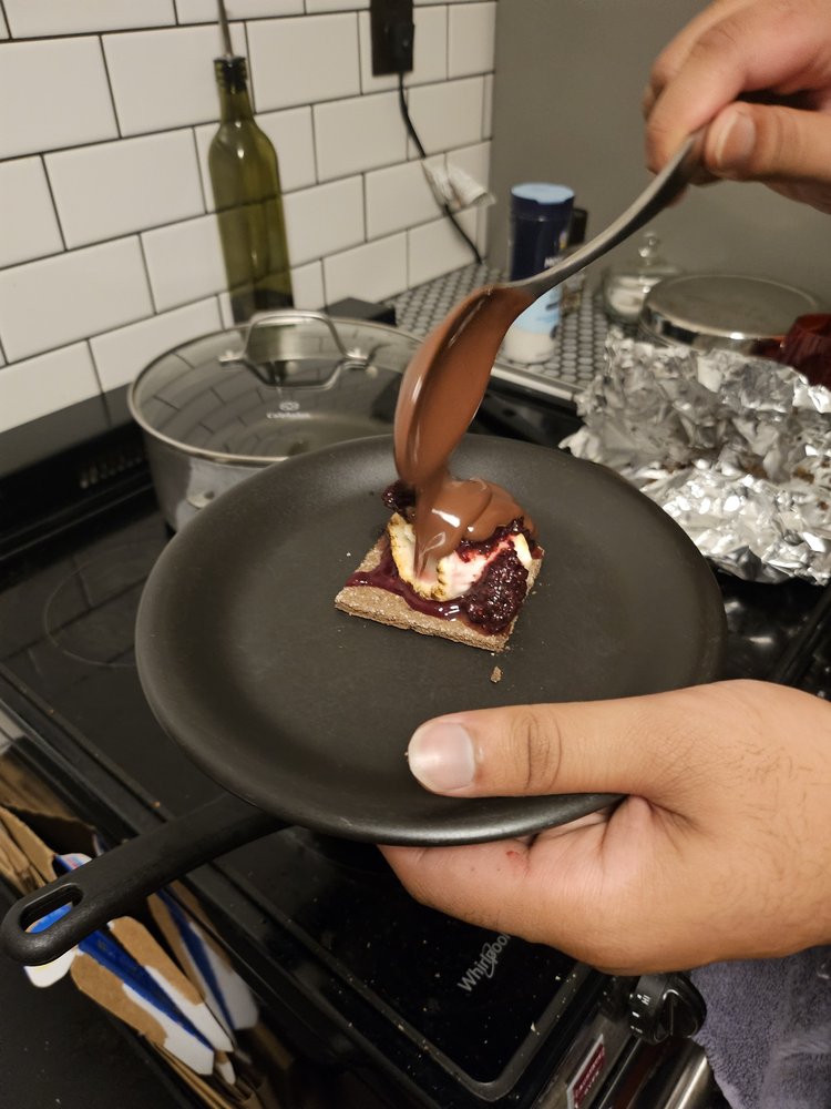 Chocolate being poured over a toasted marshmallow and jam on a graham cracker, mid-plating.
