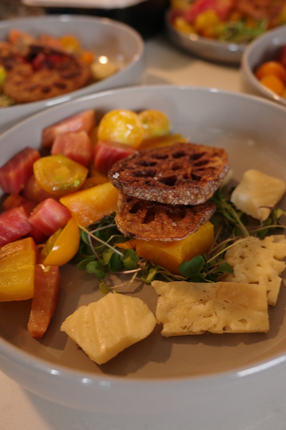 A plate of golden beets, sungold tomatoes, a parmesan crisp, microgreens, and cheese, plated with citrus.