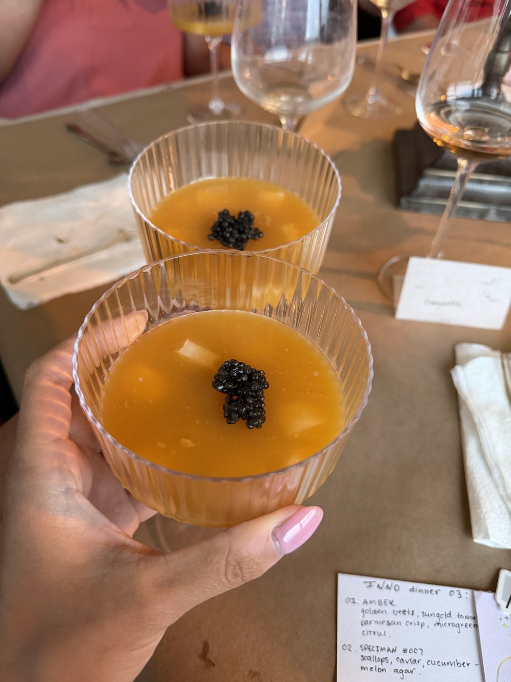 Two glass bowls of golden melon agar topped with a cluster of black caviar, held up at the table.