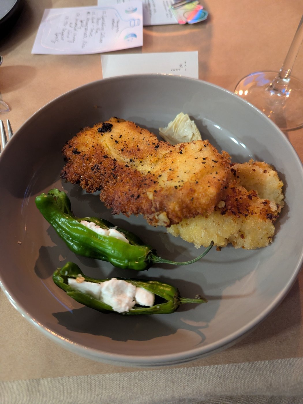 A crispy panko-breaded croquette, two goat-cheese-stuffed shishito peppers, and artichoke on a grey plate.