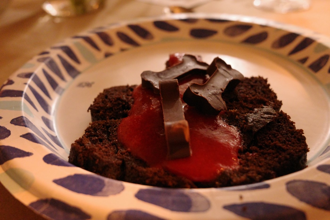 A dark chocolate cake with dinosaur-bone-shaped chocolate pieces over raspberry coulis, on a patterned paper plate.